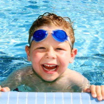 Kinderkurse bei Plitsch-Platsch, lachendes Schwimmkurs-Kind am Beckenrand